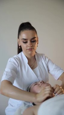 Olgun kadın müşteriye çift çene küçültme masajı yapan bir terapist. Dikey video.