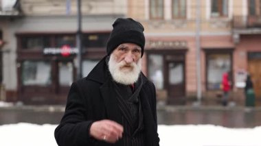 Yaşlı, düşünceli, sakallı yaşlı bir adam dikilip düşünceli bir şekilde işaret parmağını sallıyor..