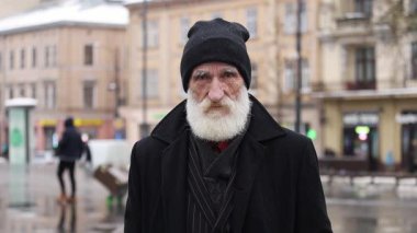 Karlı bir şehir manzarasında, uzun beyaz sakallı düşünceli yaşlı bir adam huzur içinde düşüncelere dalmış duruyor.