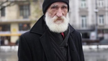 Beyaz sakallı, siyah paltolu ve şapkalı yaşlı bir adamın portresi..