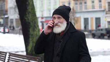 Sakallı yaşlı bir adam soğuk bir kış kentsel ortamında telefon görüşmesi yapıyor.