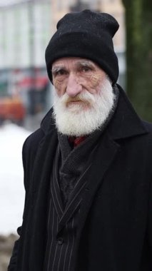 Uzun beyaz sakallı, siyah şapkalı ve ceketli yaşlı adam güzel bir kış sahnesinde duruyor..