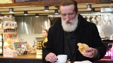 Sakallı düşünceli bir adam, rahat bir kafede kahve ve pastanın tadını çıkarıyor..