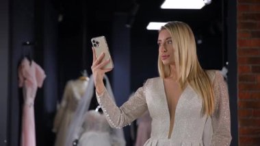Amerikan görünümlü orta yaşlı bir gelin pahalı bir moda salonunda lüks bir beyaz elbiseyle selfie çekiyor. Lüks bir gelin için gelinlik seçiyorum.