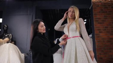 Bir gelinlik salonunda satış danışmanı, Amerikan görünümlü sarışın bir geline lüks bir beyaz elbise seçmesinde yardımcı olur. Gelin için gelinlik seçiyorum.