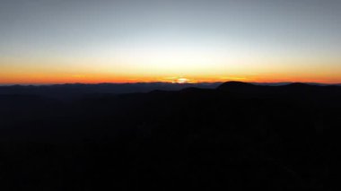 Ufuk boyunca güzel bir şekilde yayılmış canlı renkler sergilenen bir dağ gündoğumu manzarası.