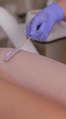 Güzellik salonunda bacak epilasyonu. Usta, spatula kullanarak saç temizleme jeli sürüyor. Dikey video.