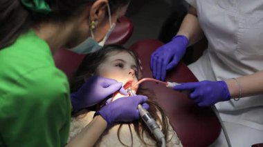 Dişçi koltuğunda yatan küçük tatlı bir kızın bebek dişlerini tedavi etme süreci. Pediatrik dişçilik bürosu. Çocukların dişlerine acısız muamele