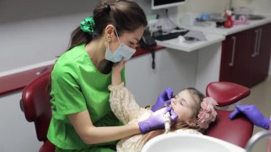 Kadın dişçi, dişçi koltuğunda yatan küçük tatlı bir kızın bebek dişlerini tedavi ediyor. Pediatrik dişçilik bürosu. Tedavi sırasında dişçi ve asistan.