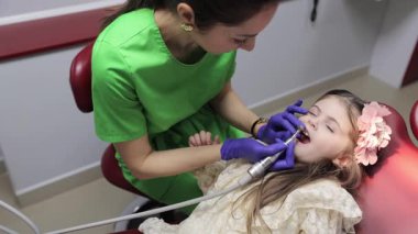 Kadın dişçi, dişçi koltuğunda yatan küçük tatlı bir kızın bebek dişlerini tedavi ediyor. Pediatrik dişçilik bürosu. Tedavi sırasında dişçi ve asistan.