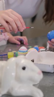 Çekici bir seramik tavşan yakınlarda otururken, eller canlı Paskalya yumurtaları boyar ve hoş bir sahne yaratır.