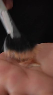 Makyaj fırçasının avuca kozmetik bir ürün uygulaması, karmaşık teknik ve sanatsallığı vurguluyor.