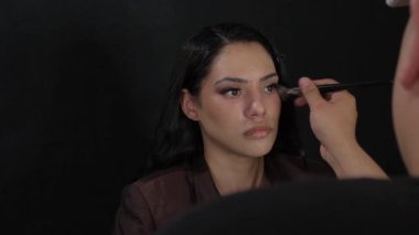 Profesyonel bir makyöz, kozmetik ürünlerini iyi tasarlanmış bir stüdyo ortamındaki bir modele ustaca uyguluyor.