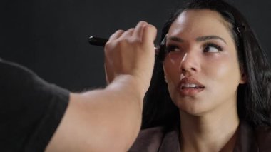 Modern bir stüdyo ortamında profesyonel makyaj uygulaması alan bir modelin detaylı yakın çekim görüntüsü