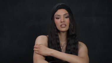 Göz alıcı ve kendinden emin bir kadın, minimalist bir ortamda inkar edilemez bir güç yayarak, büyük bir zarafetle poz verir.