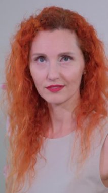 Kıvırcık kızıl saçlı, özgüven ve zarafet saçan bir kadının büyüleyici portresi.