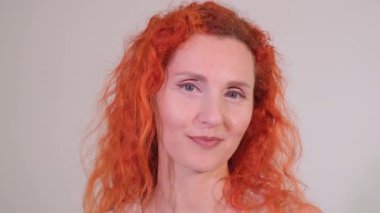 Canlı turuncu saçlı, kendine güvenen bir kadın kameraya gülümseyen, çekicilik ve yakınlık gösteren..