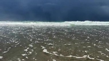 Karanlık, uğursuz fırtına bulutlarının altında şiddetle çarpan fırtınalı dalgaları canlı canlı gösteren nefes kesici bir deniz manzarası.