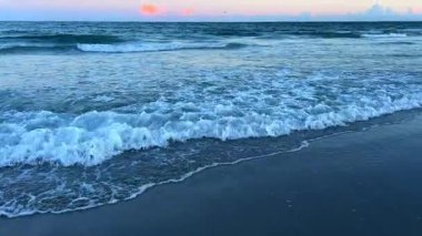 Güneş batarken, okyanus dalgaları tutkulu bir şekilde kıyıya çarpar ve manzaranın huzurlu güzelliğini gösterir..