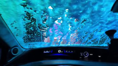 Renkli bir araba yıkama, her tarafında parlak su ve köpük lekeleri olan bir aracın içinden deneyimlenir.