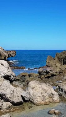 Yumuşak dalgalı kayalık bir sahil kıyı şeridinde huzurlu ve sakin bir atmosfer yaratır. Dikey video.