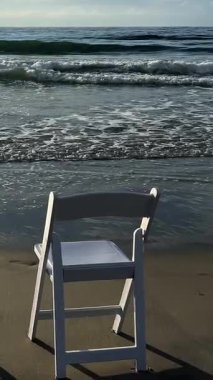 Sahilde beyaz bir sandalyenin olduğu sakin bir sahne, rahatlama ve düşünceli bir yansıma için mükemmel..