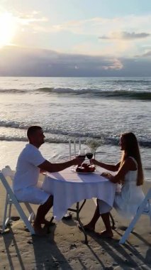 Sahilde mum ışığında romantik bir akşam yemeğinin keyfini çıkaran sevimli bir çift gün batımına karşı bardaklarını kaldırıyor..