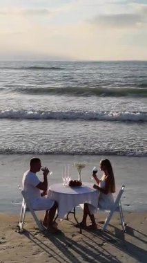 İki kişilik büyüleyici bir plaj yemeği. Ufukta büyüleyici bir günbatımı ve dingin okyanus dalgaları var..