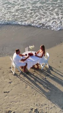 Deniz kenarında sıcak bir akşam yemeğinde güzel bir gün batımında eğlenen bir çift var..