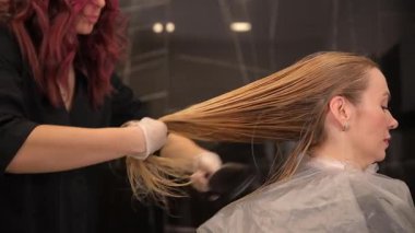 Çağdaş bir kuaför ortamında, yetenekli bir stilist bir seans sırasında bir müşterinin saçına dikkatlice renk uygular