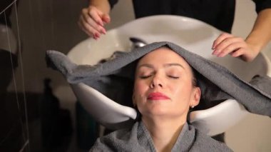 Bir kadın, bir kuaförde rahatlatıcı bir saç tedavisinden zevk alır. Etrafı profesyonellerle çevrili ve rahatlatıcı bir ortam içindedir..
