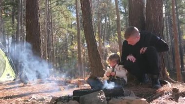 Huzurlu ve huzurlu bir ormanda, sıcak bir kamp ateşinin etrafında toplanan aile içi bir an.