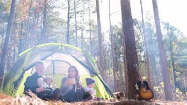 İki çocuklu canlı bir aile ormanda kamp yapmanın keyfini çıkarıyor. Gitarla eğleniyorlar..