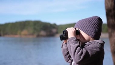 Bir çocuk huzur dolu bir göl kenarında dürbünle doğayı keşfeder. Dünya hakkında macera ve merak taşır.