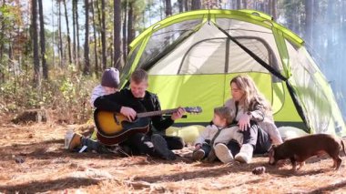Neşeli bir aile, ormanda kamp yaparken kamp ateşinin yanında müzik dinleyerek vakit geçiriyor..