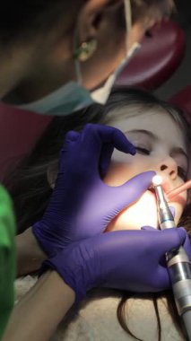 Genç bir kız, profesyonel bir klinikte detaylı muayene olurken dişçi koltuğunda oturur. Dikey video.