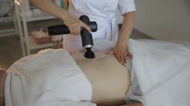 Masör, karın bölgesini rahatlatıcı bir ortamda etkili bir şekilde tedavi etmek için masaj silahı kullanır..