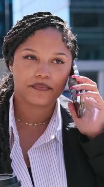 Enerji ve hareketle dolu kalabalık bir şehir ortamında dikilen Afro-Amerikalı bir kadın telefonda konuşuyor. Dikey video