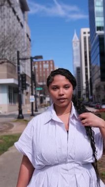 Zarif bir Afro-Amerikan iş kadını çağdaş mimariyle çevrili modern bir şehirde güvenle yürüyor. Dikey video