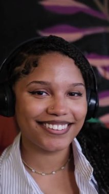 Kulaklıklı gülümseyen bir Afrikalı Amerikalı kadın yaratıcılığı ve pozitifliği arttırmak için tasarlanmış parlak ve ilham verici bir çalışma alanının tadını çıkarıyor. Dikey video