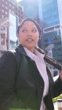 Afro-Amerikalı bir kadın, sıcak güneş ışığıyla güzelce aydınlatılmış canlı bir şehir ortamında kendine güvenerek duruyor. Dikey video