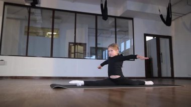 Genç bir çocuk, parlak ışıklandırılmış bir dans stüdyosunda zahmetsizce ayrılırken etkileyici esneklik sergiliyor..