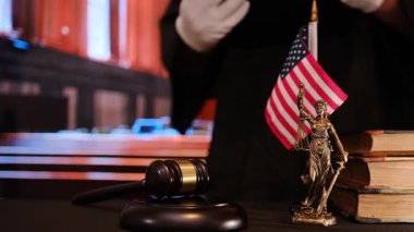 Bir tokmak, bir Adalet Heykeli ve kanun ve düzeni simgeleyen bir Amerikan bayrağı tasvir eden ayrıntılı bir mahkeme sahnesi.