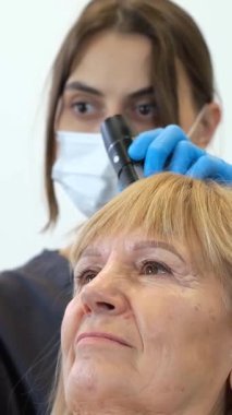 Bir dermatolog güçlü bir mikroskop kullanarak hastanın kafa derisini dikkatlice inceler..