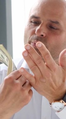 Gıcır gıcır beyaz gömlekli bir adam nakit sayıyor, şık bir ofiste para yönetimine dikkatini gösteriyor.