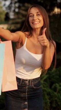 Neşeli bir kadın canlı alışveriş torbalarını gururla sergiliyor, güneşli bir ortamda saf mutluluk yayıyor..