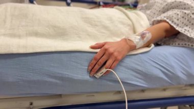 Hastane kıyafeti giymiş bir hasta serumla yatakta rahat bir şekilde dinlenirken tıbbi tedavi görüyor.