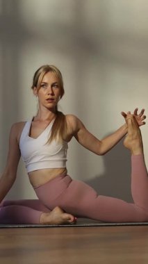 Güzel bir Amerikalı kadının portresi. Güneş ışığında evde yoga yapıyor. Dikey video. 