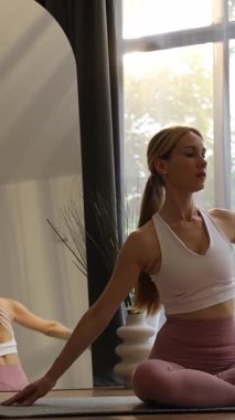 Evde sabah yogasında esneme hareketleri yapan odaklanmış genç sarışın kadın. Dikey video.