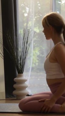 Genç Avrupalı bir kadın evinde yoga yapıyor. Dikey video. 